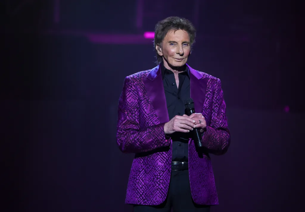 Barry Manilow in a textured purple jacket, holding a microphone.