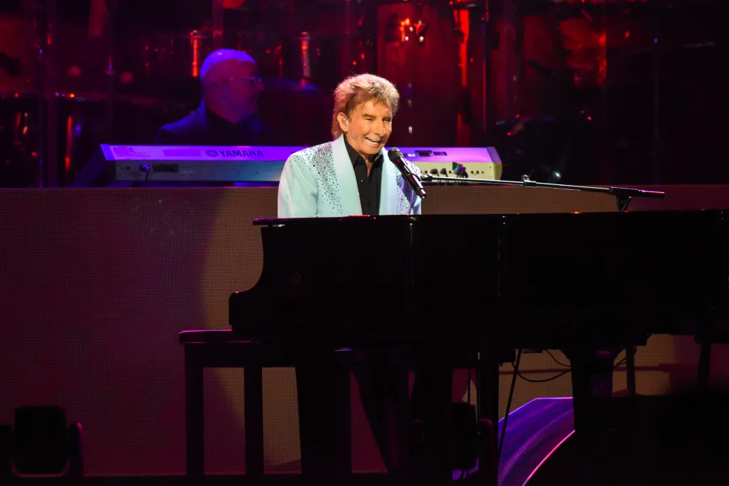 Barry Manilow performing at a piano on stage.