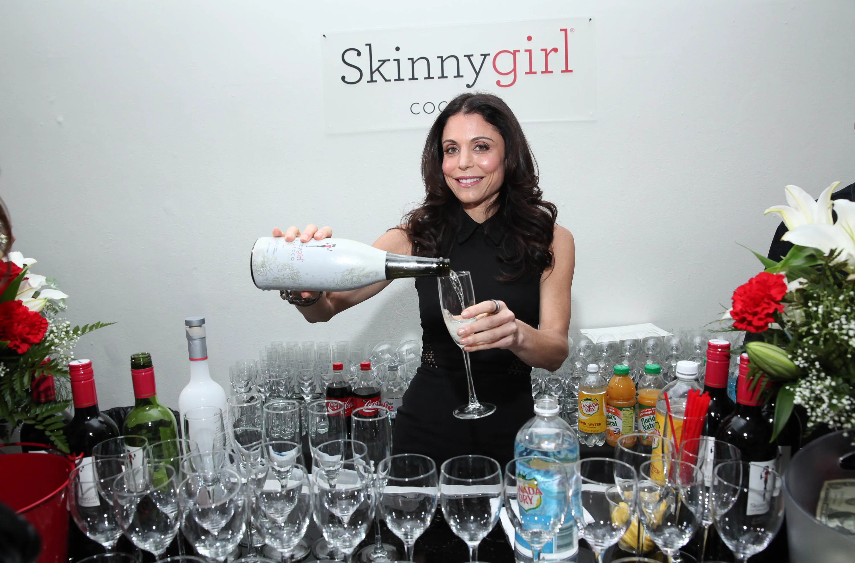 Bethenny Frankel pouring Skinnygirl Prosecco at a bar with various drinks and glasses.