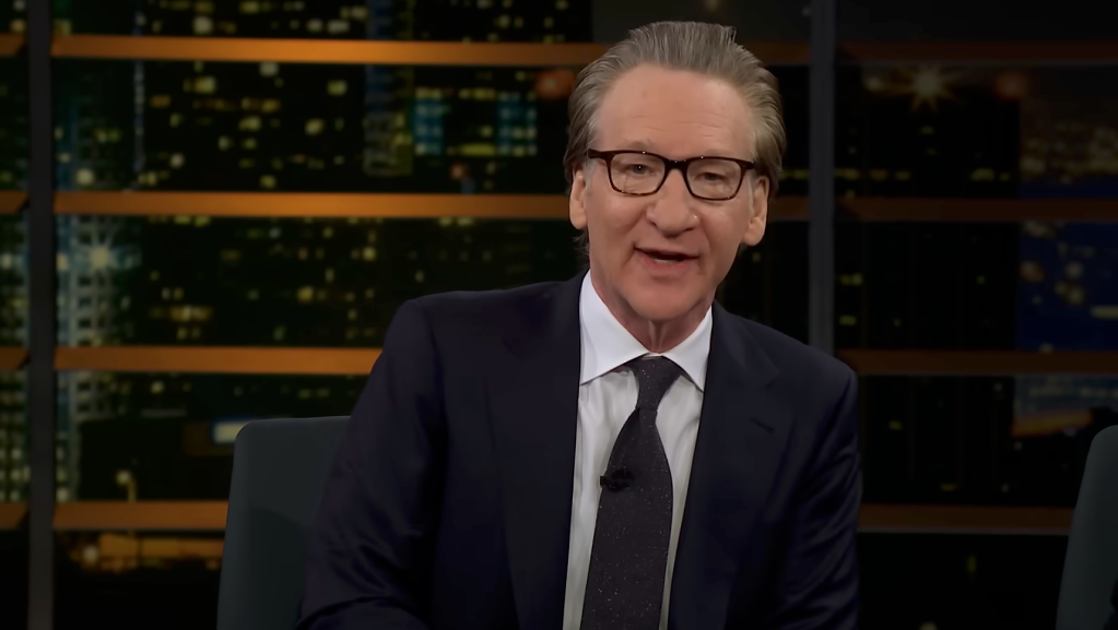 Bill Maher speaking with a city skyline in the background.
