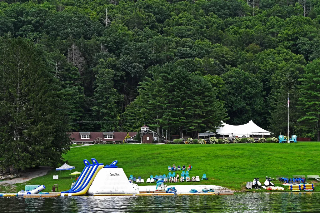 Camp Getaway resort by a lake with a water slide, tents, and a wooded hillside.