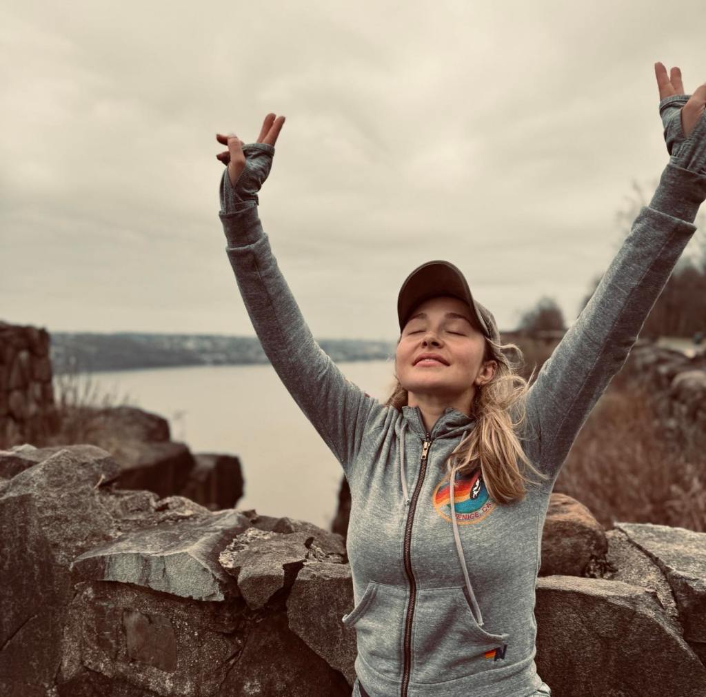 Hayden Panettiere with her arms raised on a rocky overlook.
