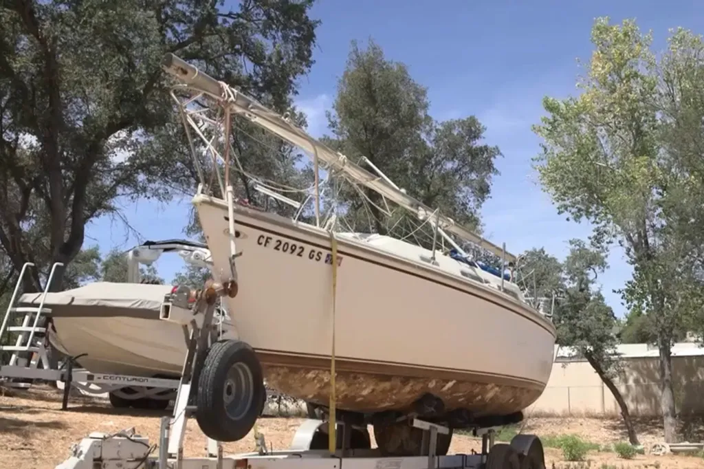 A boat with an accumulation of golden mussels on its hull, sitting on a trailer.