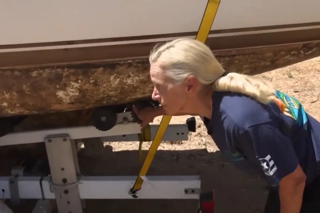A blonde woman points to golden mussels stuck to the underside of a boat.