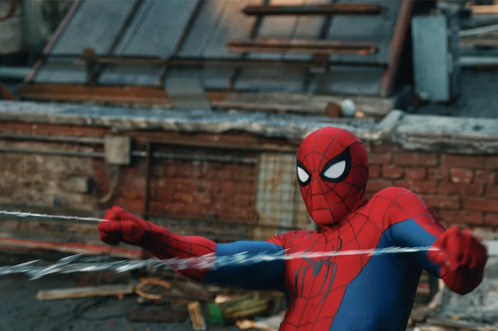 Spider-Man swinging with a web, against a brick building.