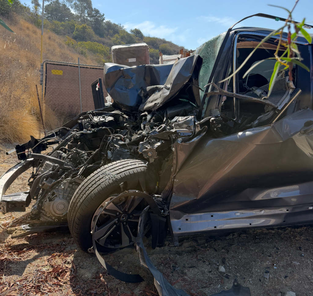 The heavily damaged front of a dark gray car after a serious collision.