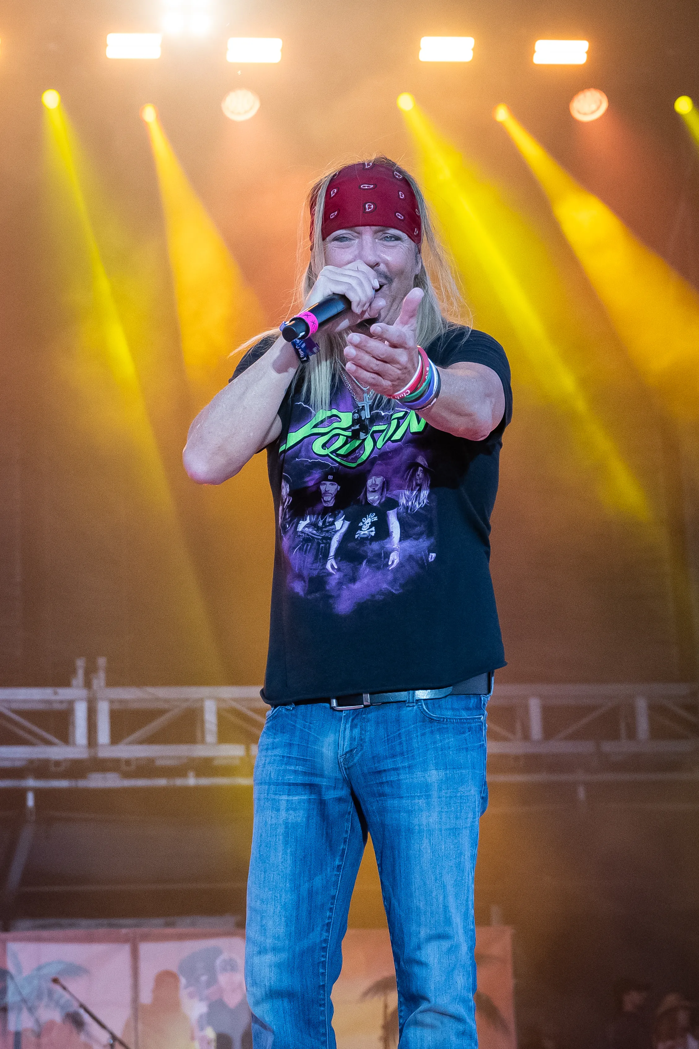 Bret Michaels of Poison performs onstage wearing a black t-shirt, jeans, and a red bandana.