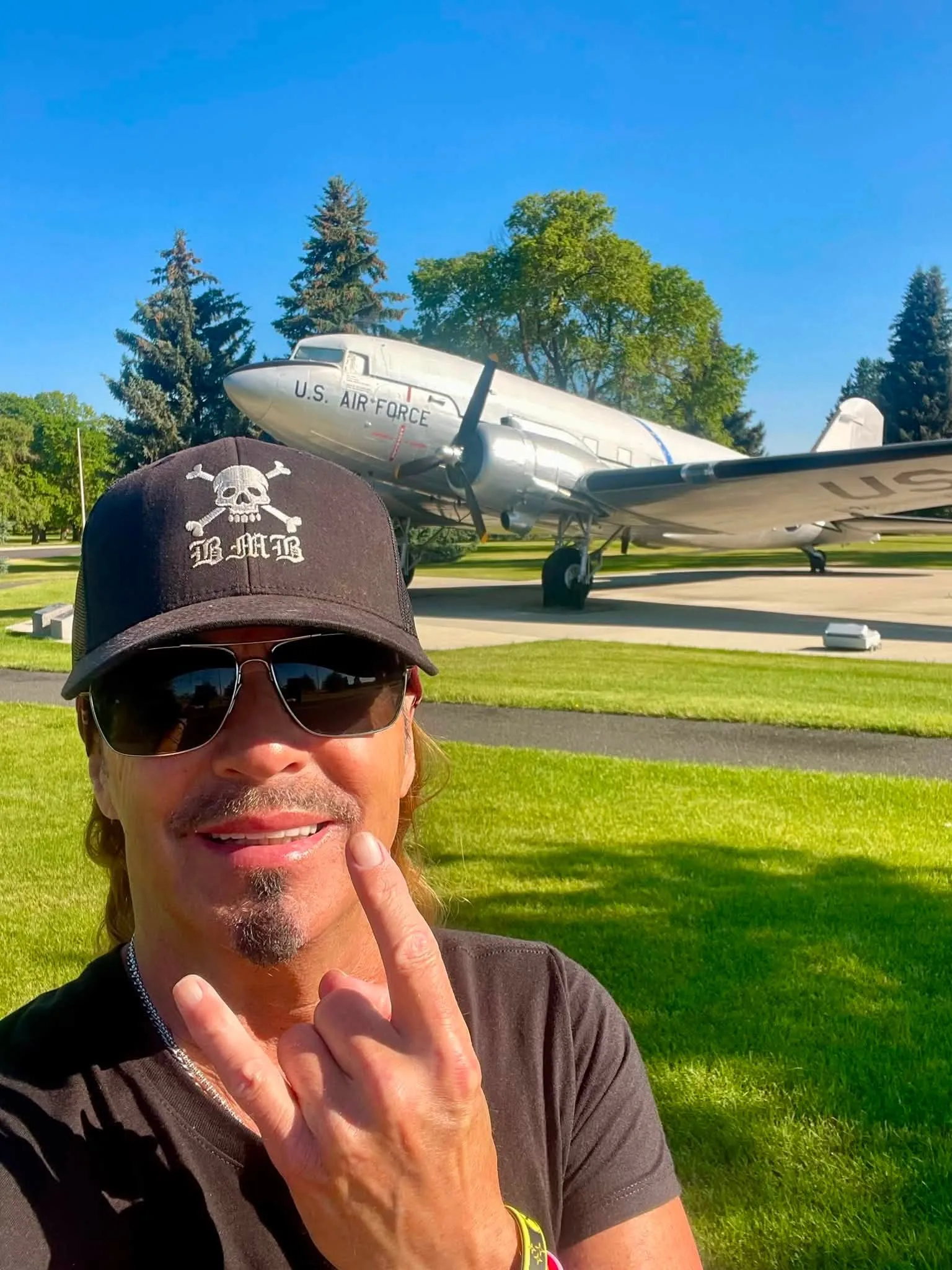 Bret Michaels taking a selfie and making a rock and roll hand gesture in front of a U.S. Air Force plane.