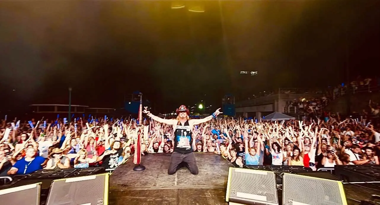 Bret Michaels on stage with a large crowd in front of him.