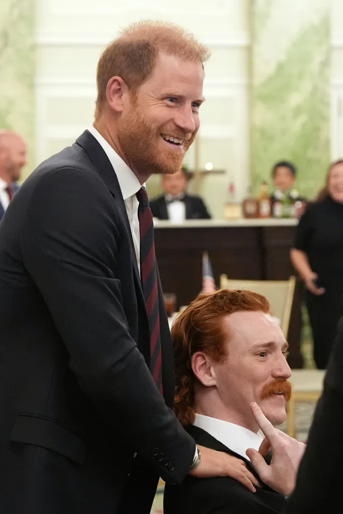Prince Harry smiling while touching the shoulder of William Bringer, who has red hair and a mustache.