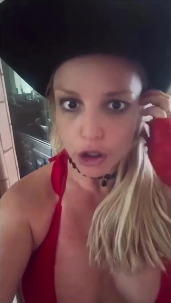 Britney Spears in a red top and black cowboy hat with a droopy left eye.