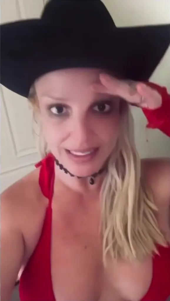 Britney Spears in a black hat and red top, saluting the camera.