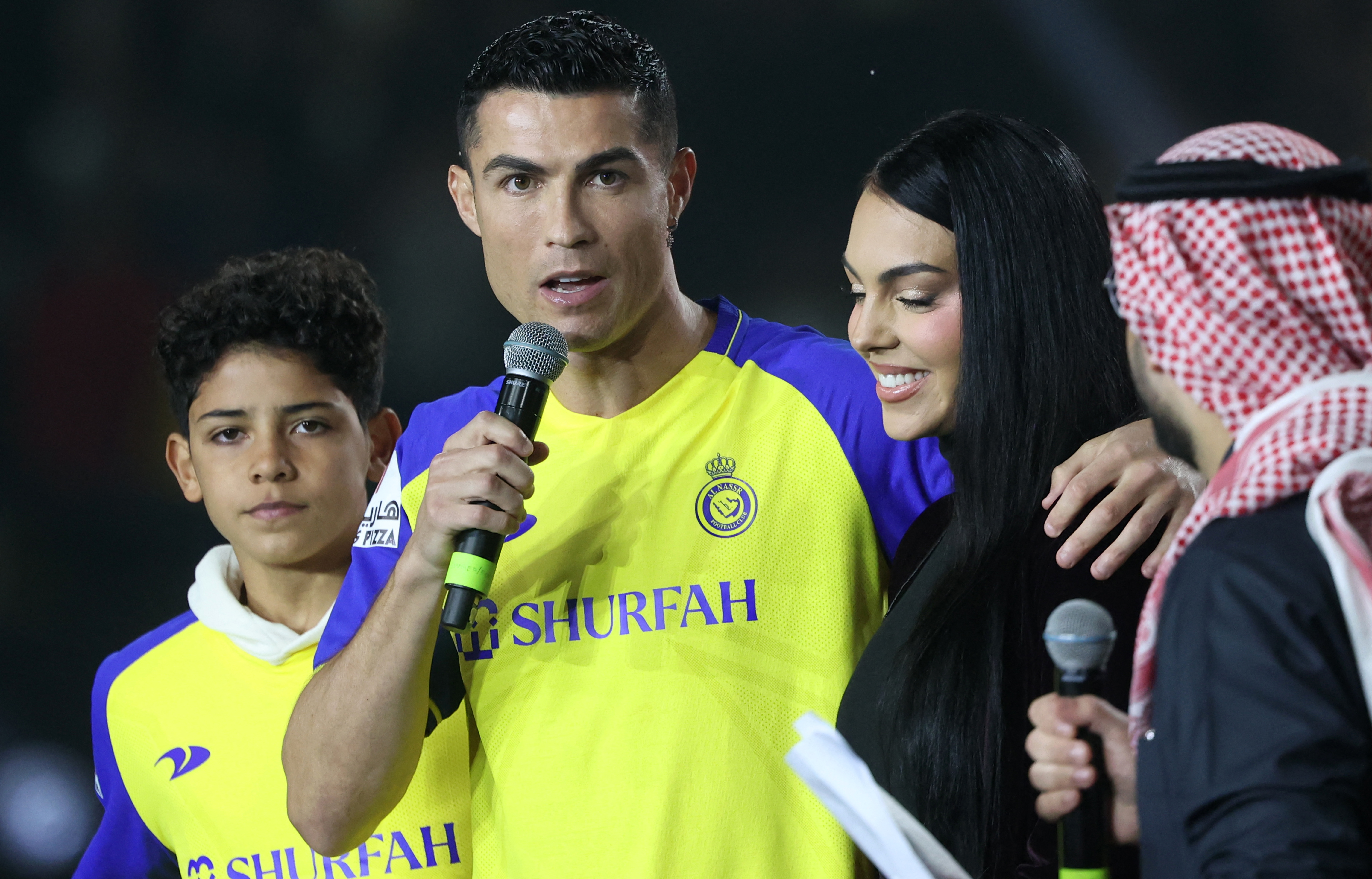 Cristiano Ronaldo speaks into a microphone, flanked by Georgina Rodriguez and his son.