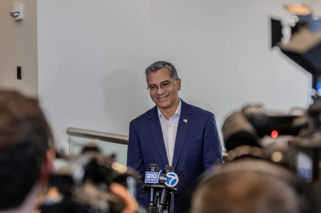 Xavier Becerra smiling while speaking to reporters.