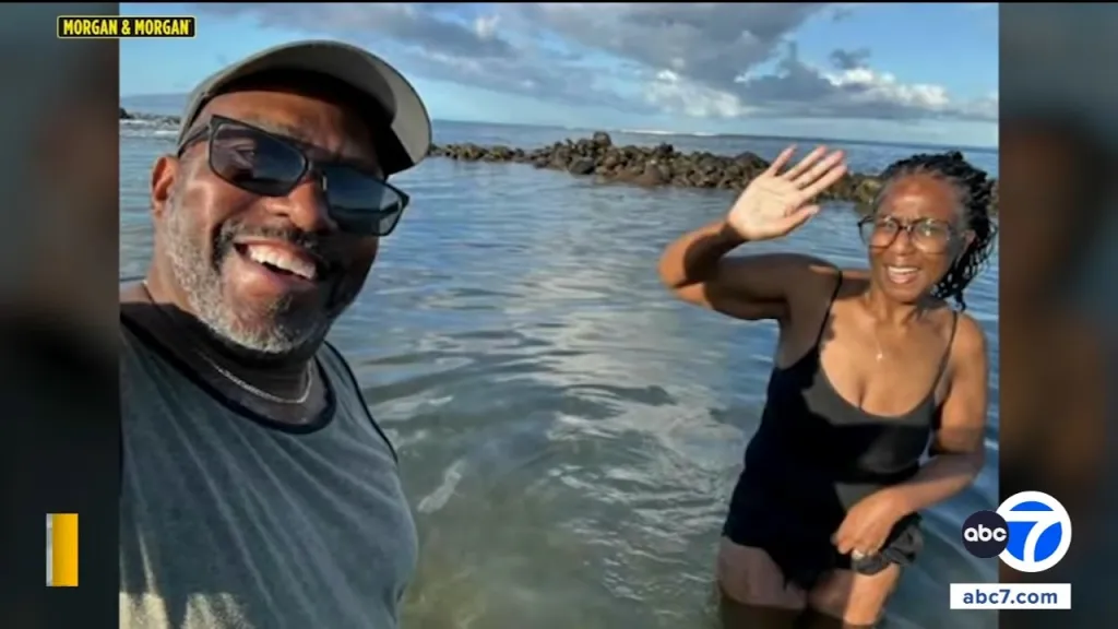 A man and woman standing in water, smiling and waving.