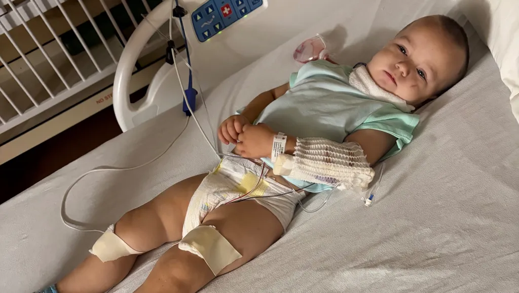 A baby lies in a hospital bed with medical sensors and bandages.