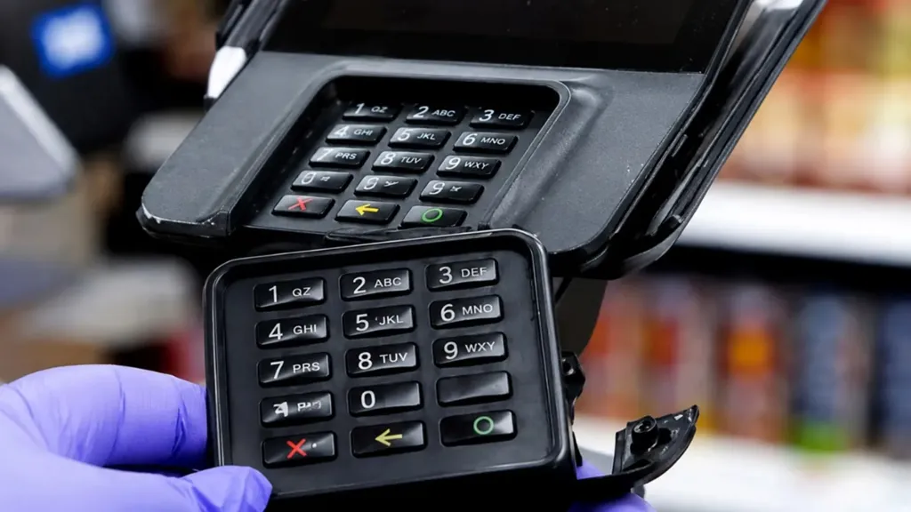 A gloved hand removes a skimming device from a credit card reader.