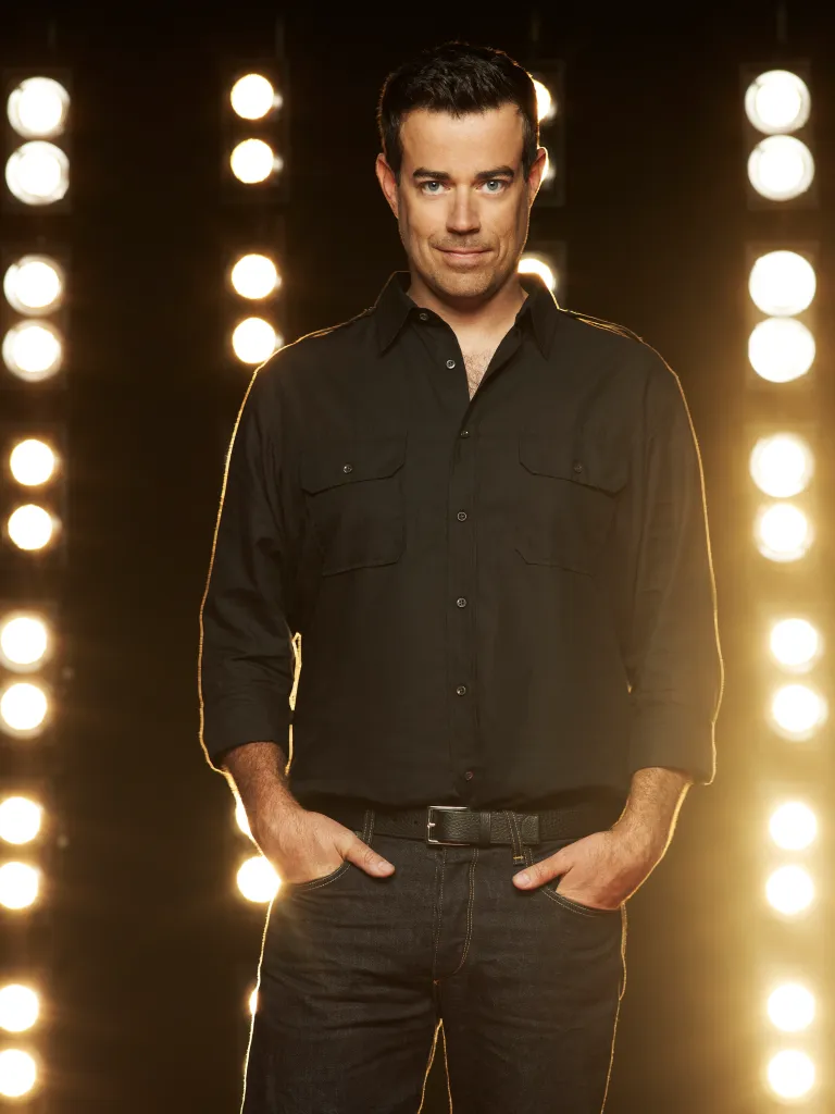 Carson Daly, host of The Voice, poses for a half-length portrait with a wall of lights in the background.