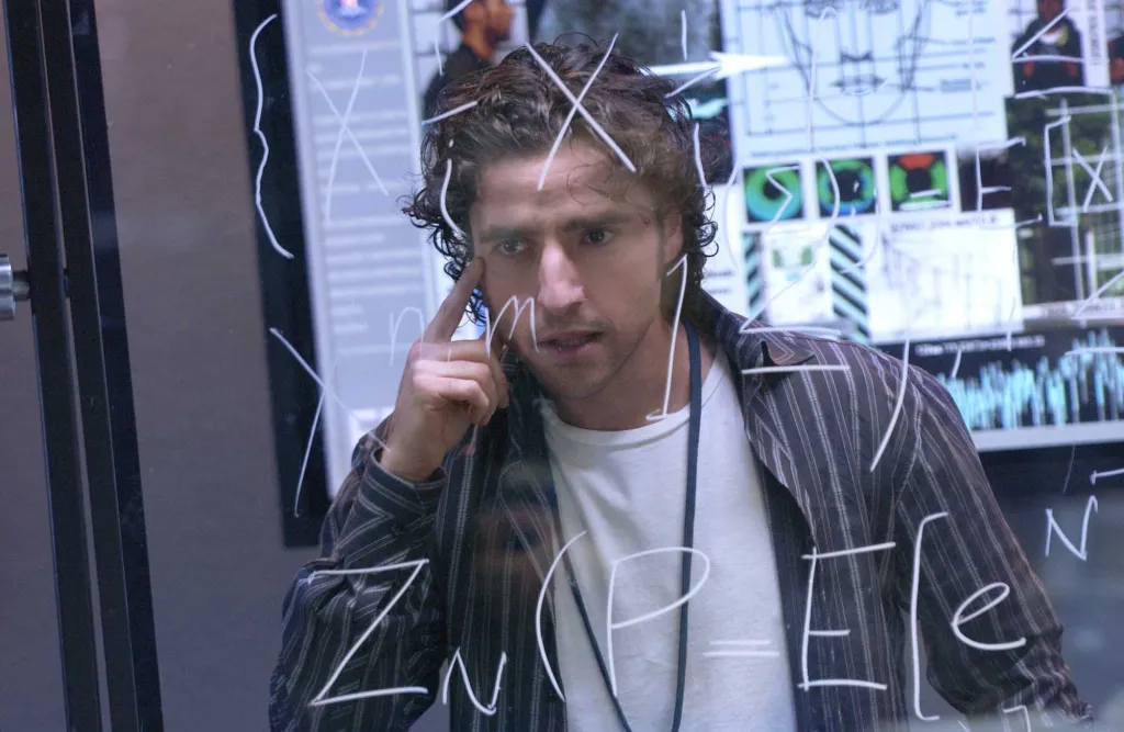 David Krumholtz as Charlie Eppes from the TV show Numb3rs, looking intently at mathematical equations on a transparent board.