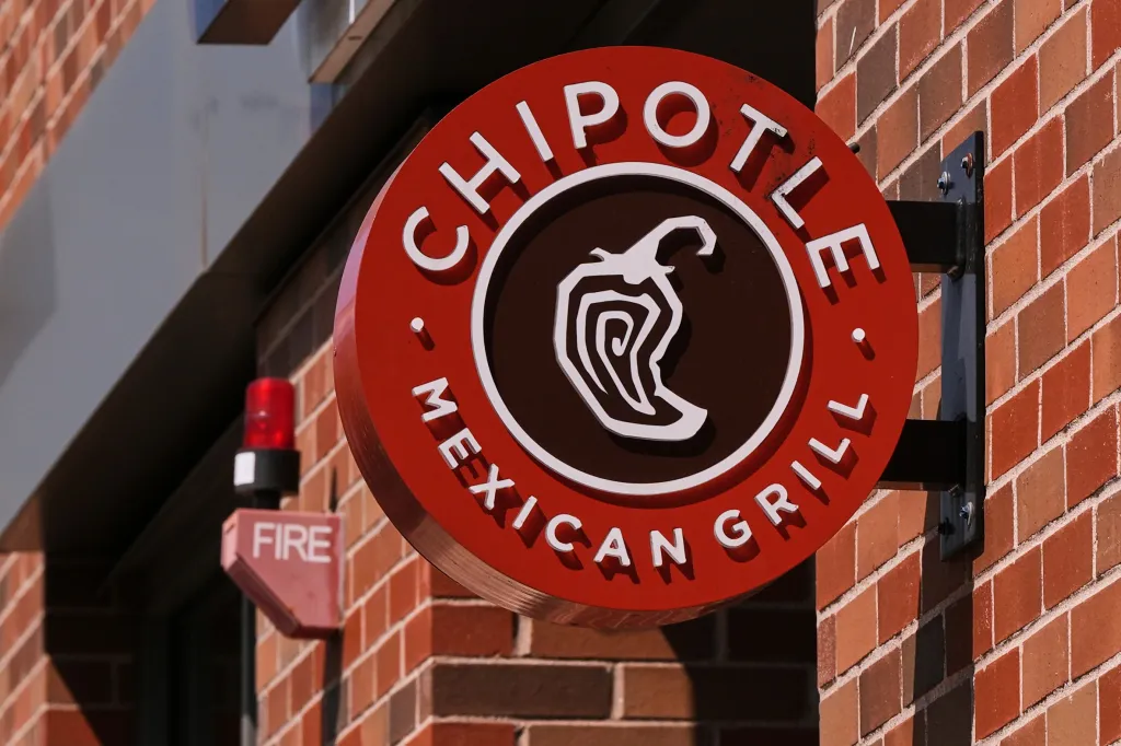 The red Chipotle Mexican Grill logo with a chili pepper in the center, mounted on a brick wall.