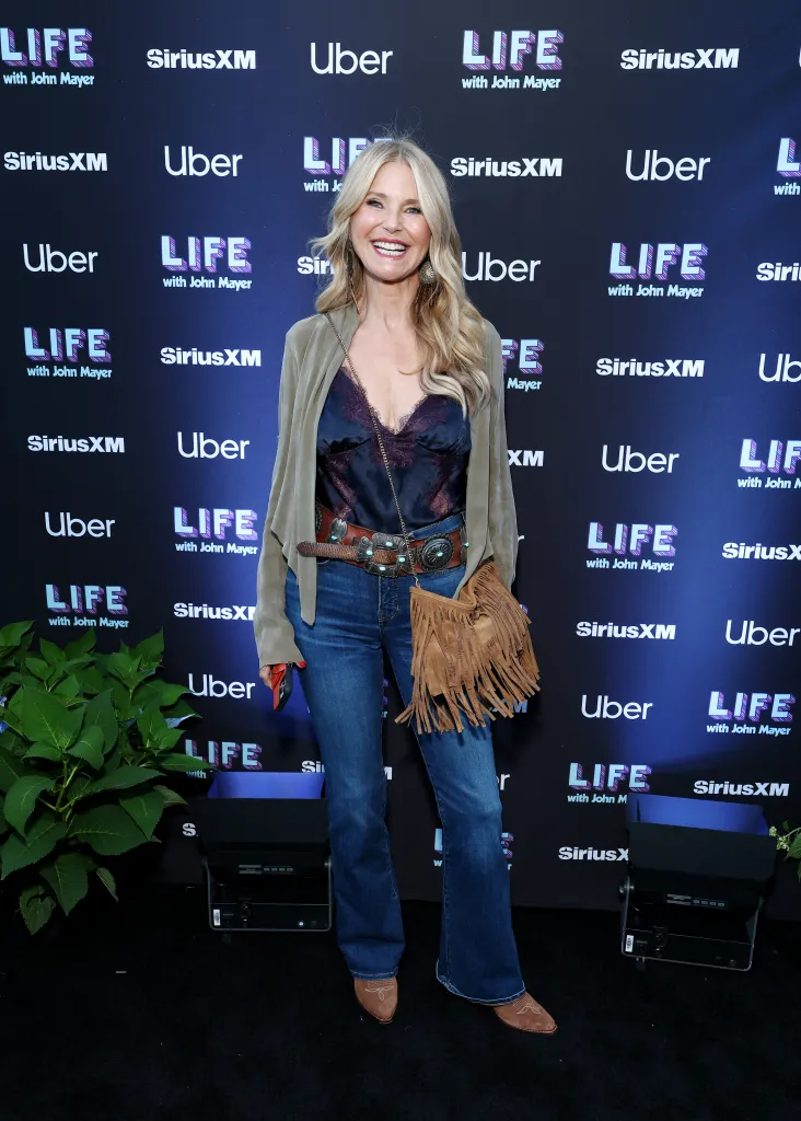 Christie Brinkley smiles while posing for a photo in front of a step-and-repeat banner.