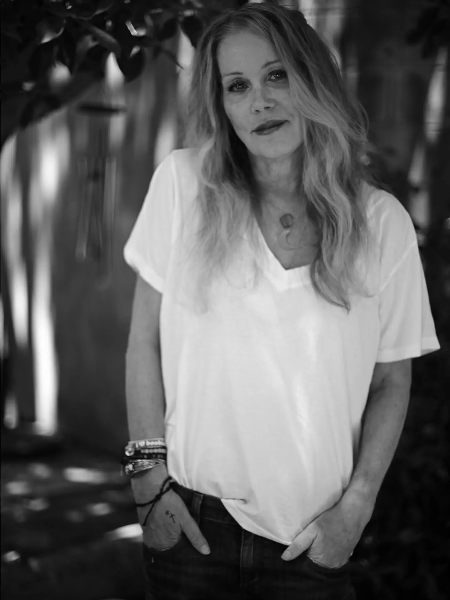 Black and white photo of Christina Applegate, a woman with long hair and a light shirt, hands in her pockets, looking at the camera.