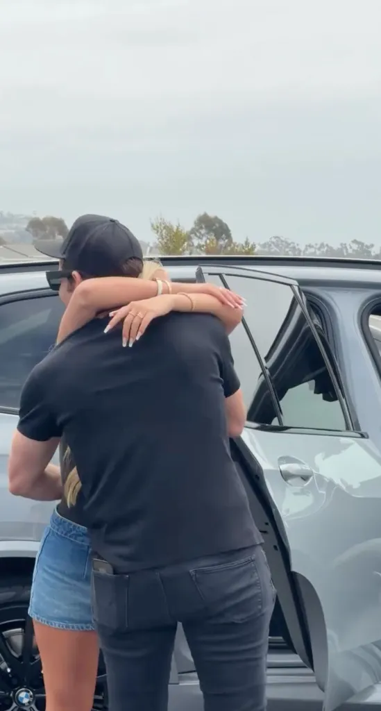 Christina Haack hugging Tarek El Moussa beside a car.