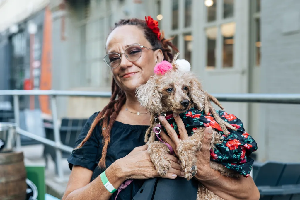 Christine Perea holds her poodle, Bunny, wearing a floral coat and two pom-poms on its head.