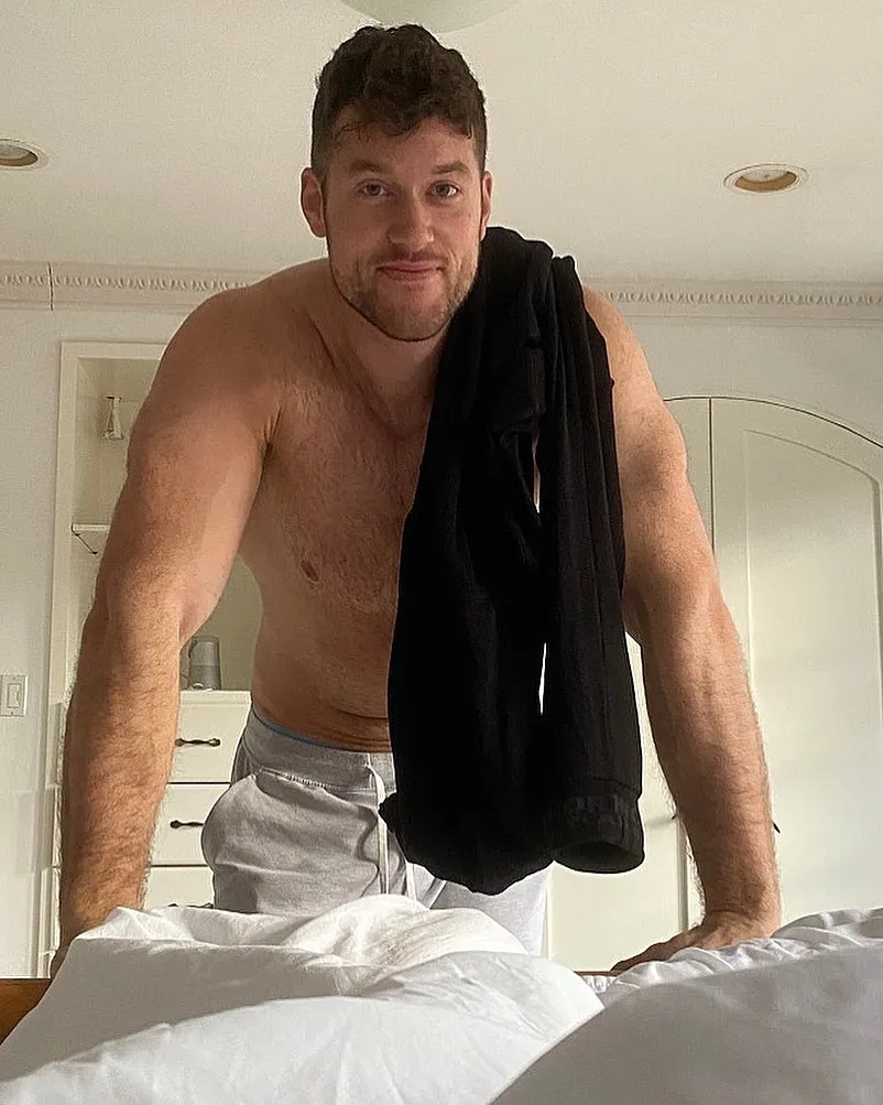 Clayton Echard, shirtless, leaning over a bed.