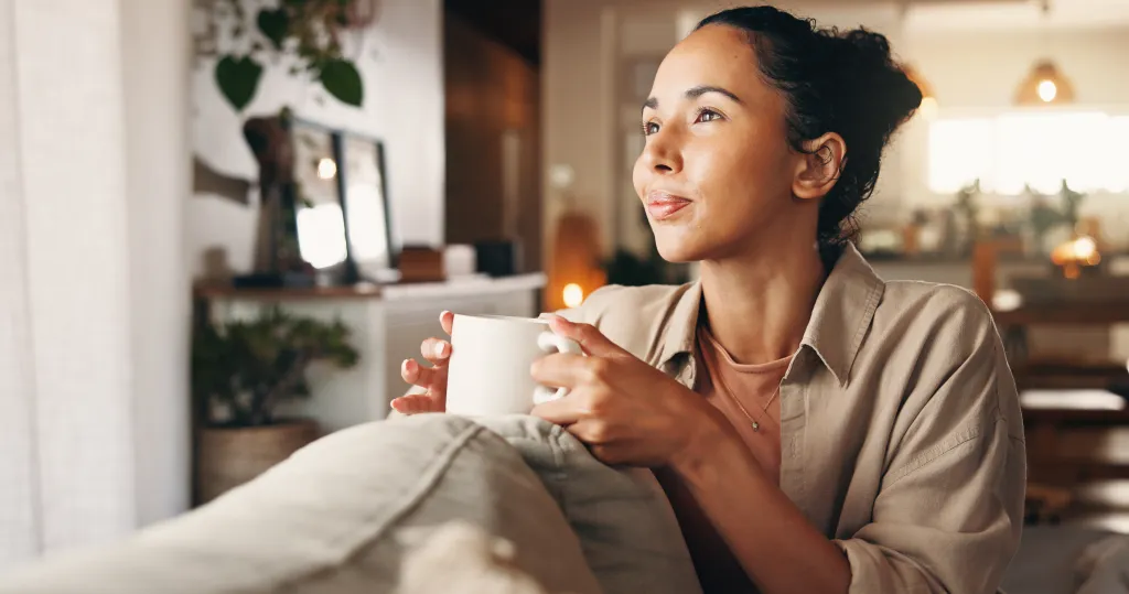 A woman relaxing on a sofa with a coffee mug, looking up and to the right.