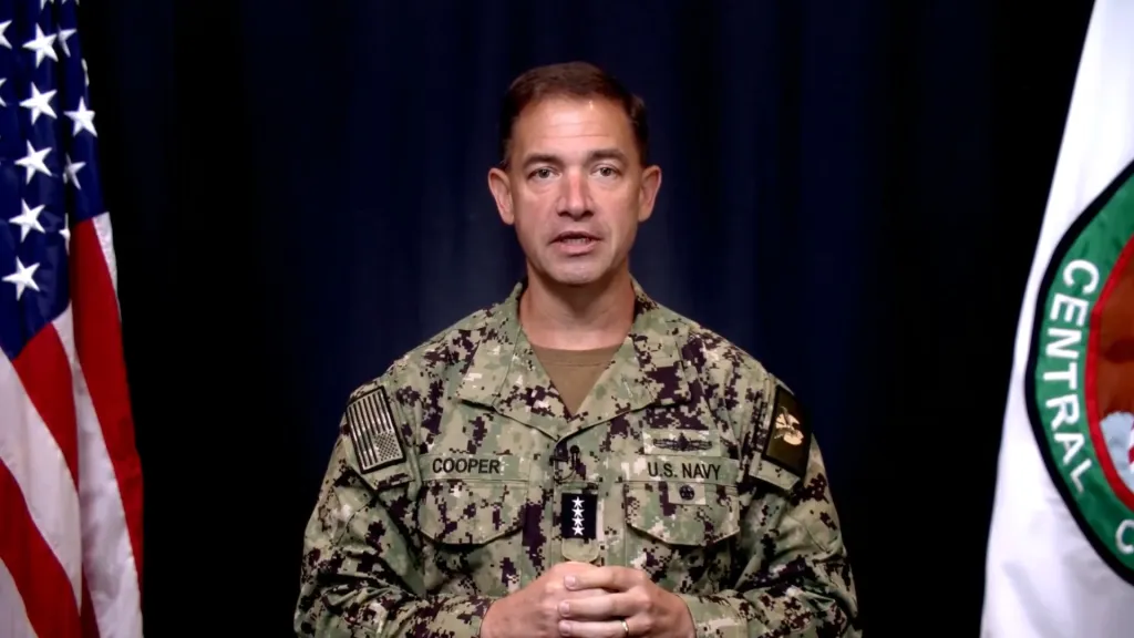 Admiral Brad Cooper, commander of CENTCOM, in his uniform, speaks to the camera with a US flag and the CENTCOM flag in the background.
