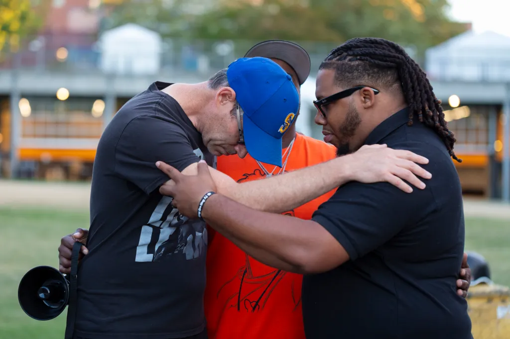 Three men huddle together in prayer at a vigil.