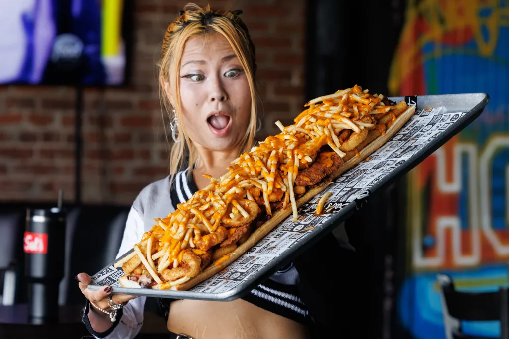 Competitive eater Raina Huang holds a large sandwich loaded with fries and sauce.