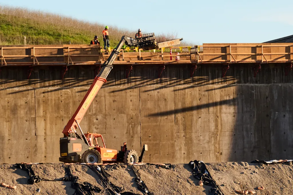 Construction crews loading pallets of native plants onto the Wallis Annenberg Wildlife Crossing over U.S. Highway 101.