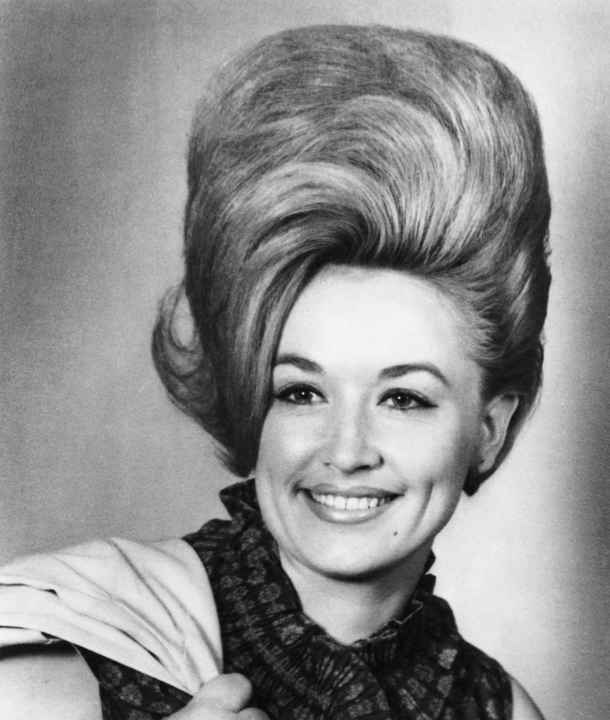 Dolly Parton in a black and white photo, wearing a ruffled top and big hair.
