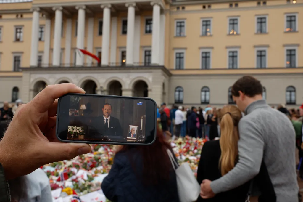 A man watches King Haakon VIII's speech on his phone at a memorial for King Harald V.