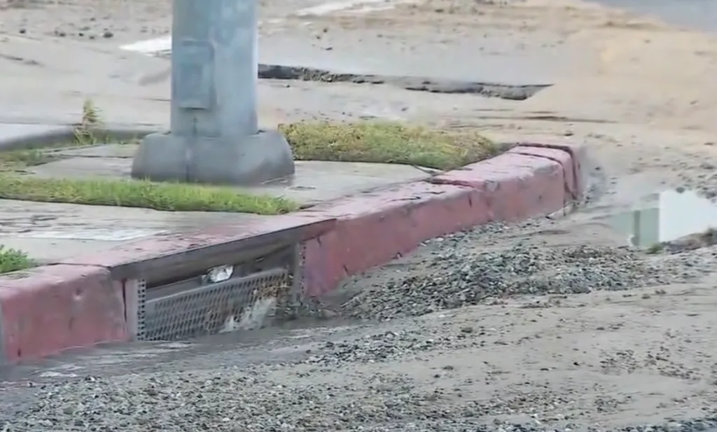Water rushes into a storm drain on a street.