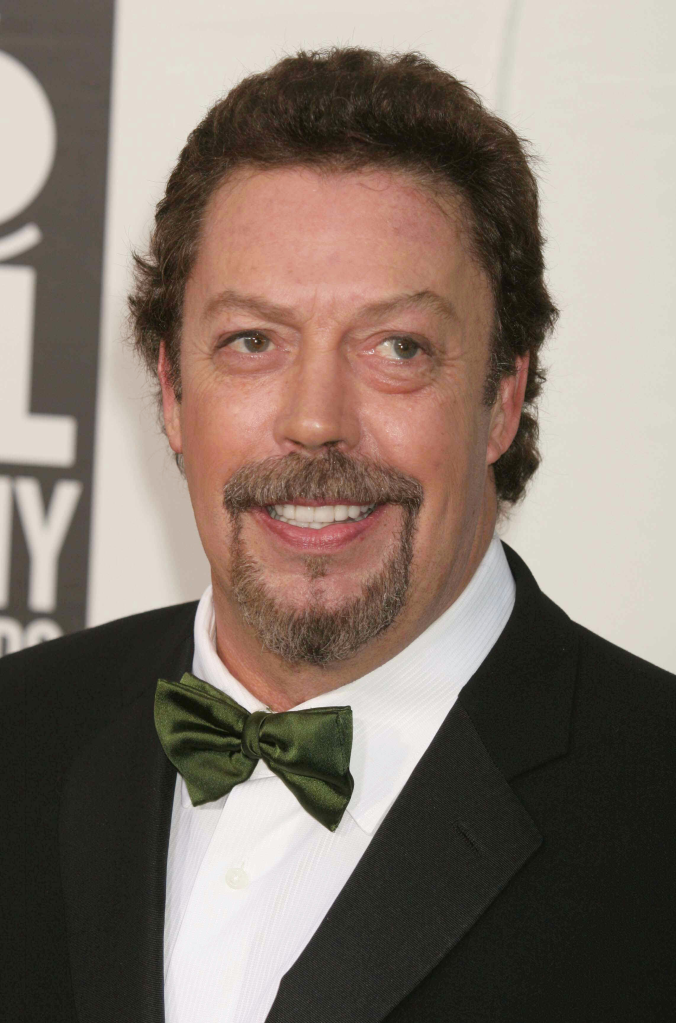 Tim Curry smiling while wearing a tuxedo and green bow tie.