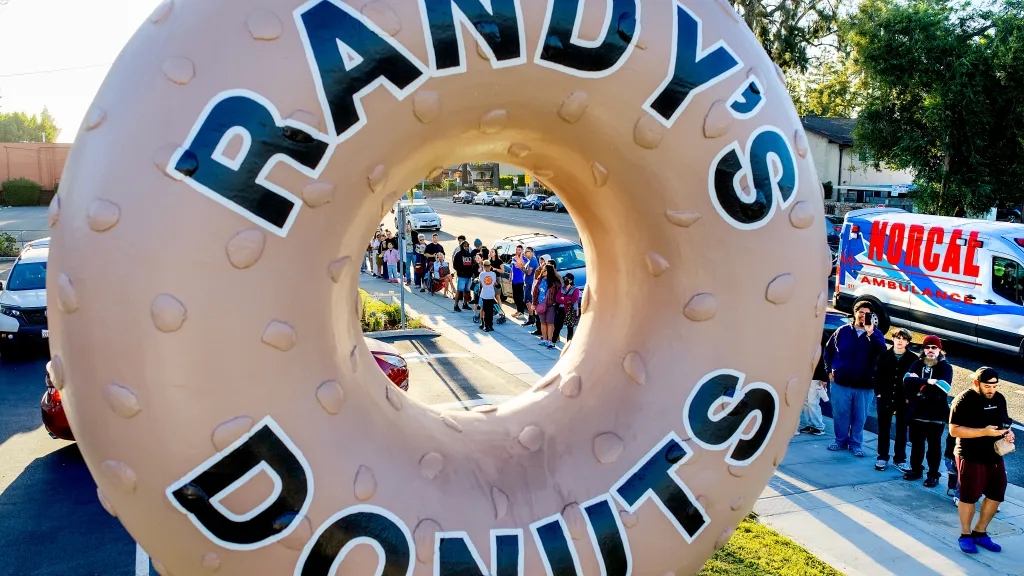 Customers lining up for the grand opening of Randy's Donuts in Santa Clara, California, seen through the giant donut sign.