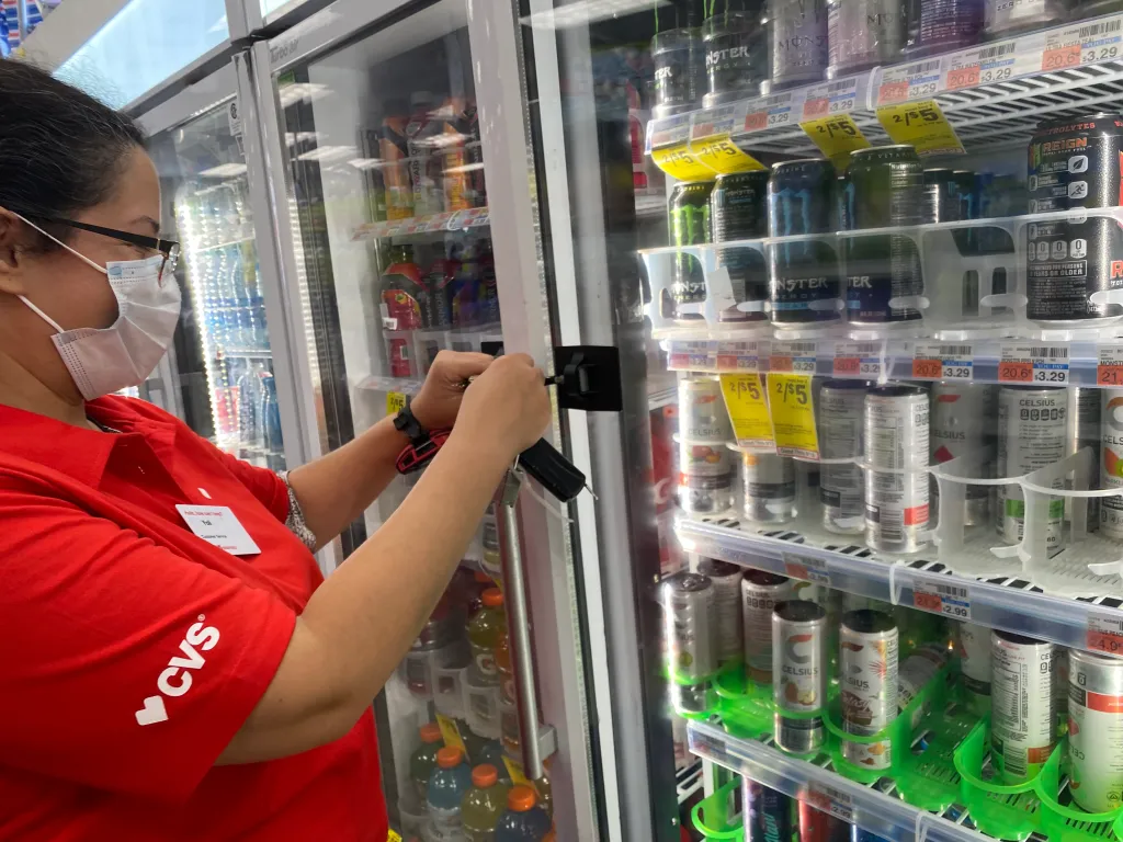 A CVS Pharmacy employee unlocks a refrigerator to access an energy drink.