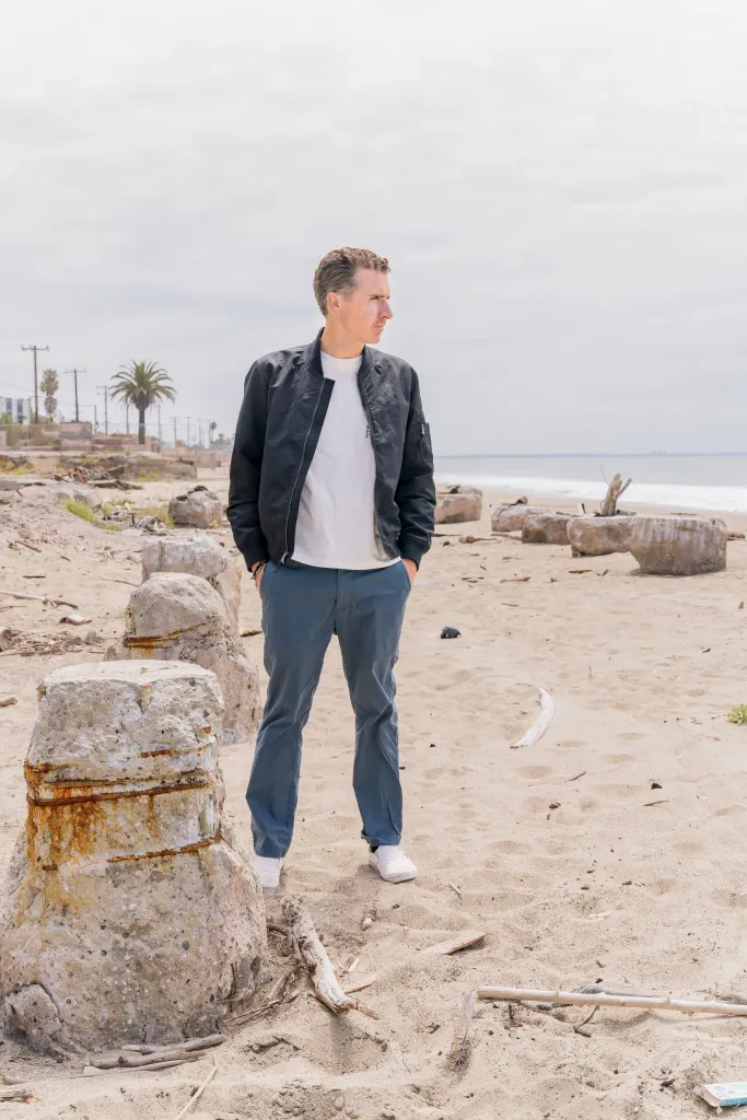 Daniel Smith standing on a sandy beach with large concrete debris, looking towards the ocean.