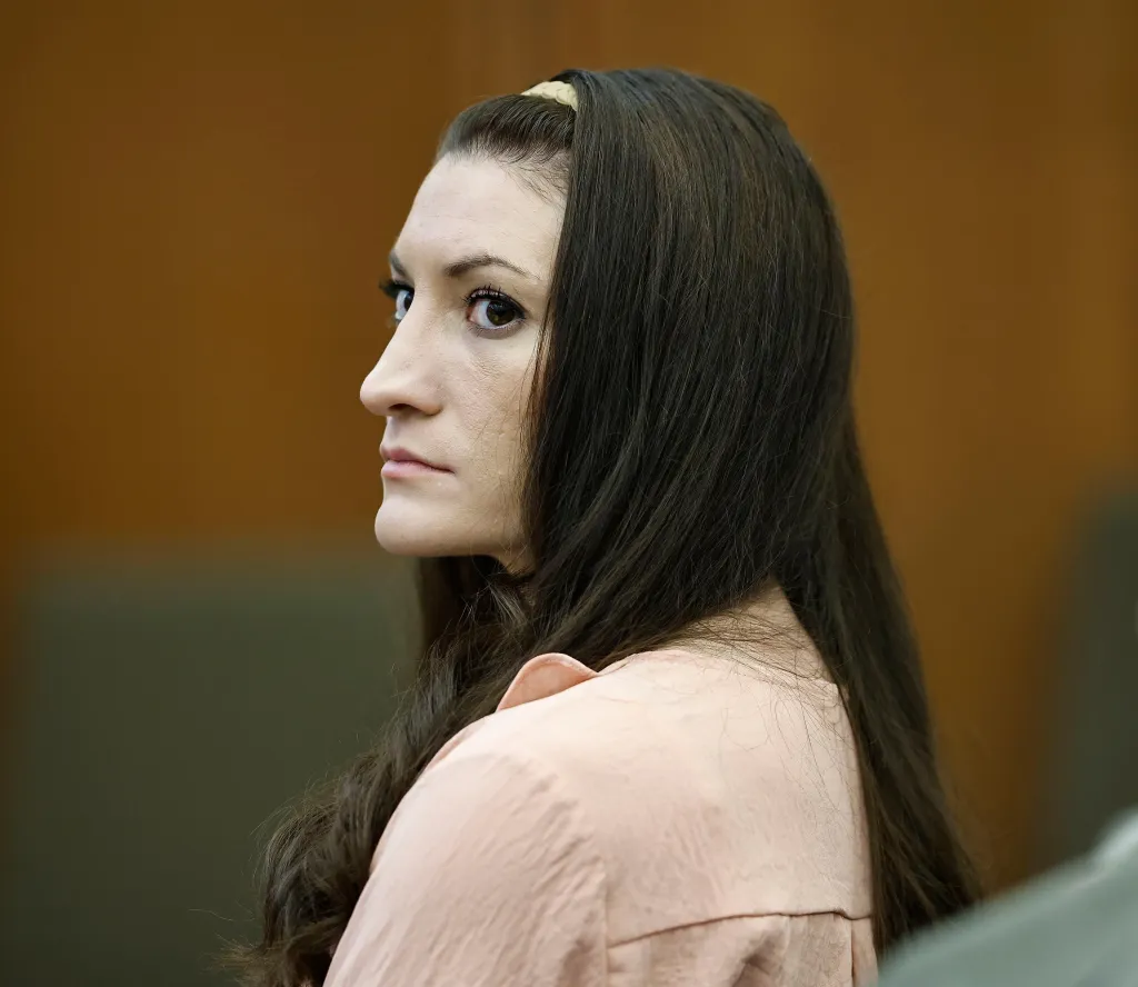Lindsay Clancy at her murder trial, wearing a light pink shirt, with long dark hair, looking to the left with an attentive expression.