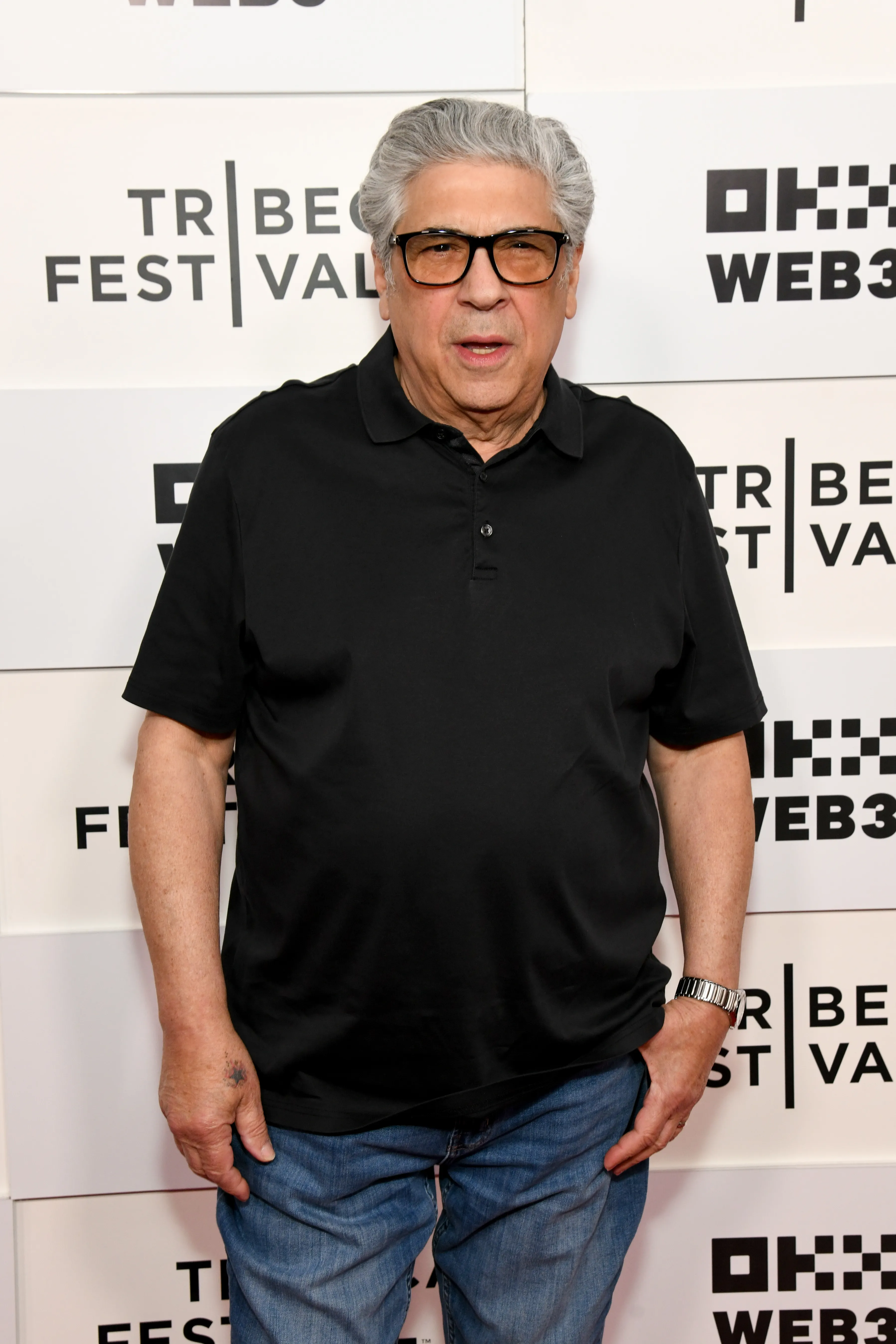 Vincent Pastore poses in a black polo shirt and blue jeans at the