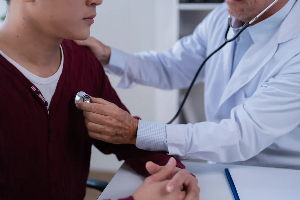 Doctor checking a young man's chest with a stethoscope.