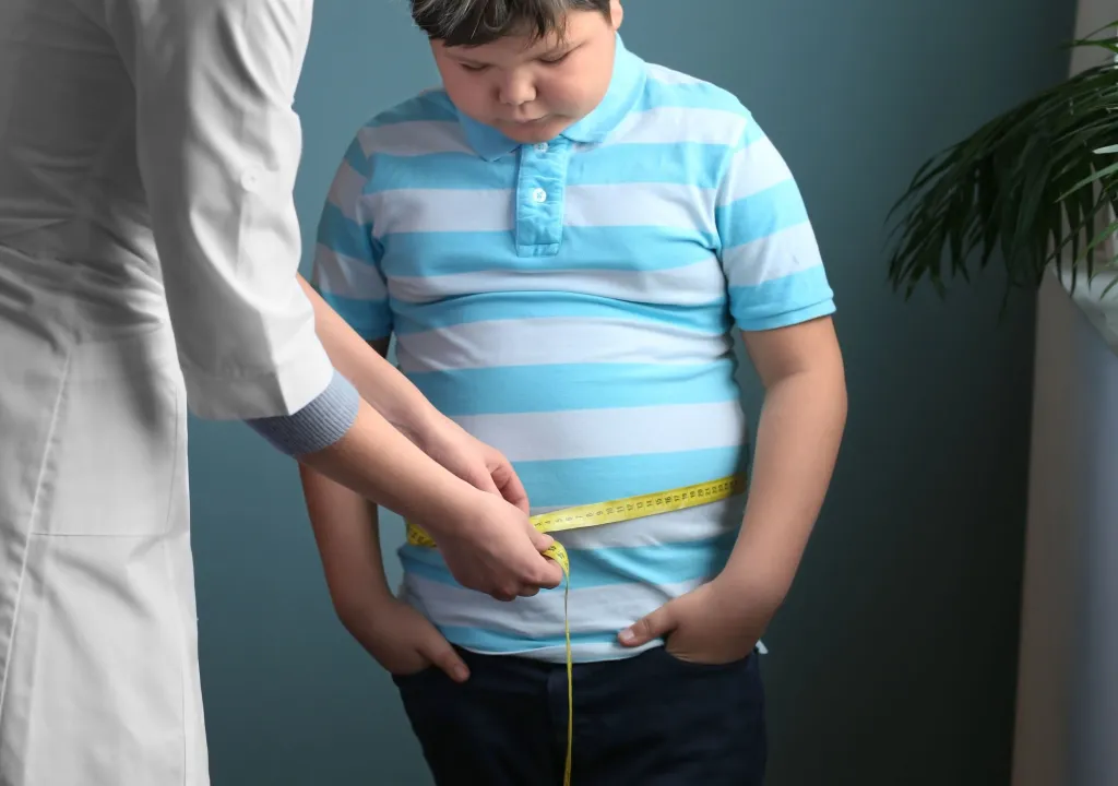 Doctor measuring the waist of an overweight boy with a tape measure in a clinic.