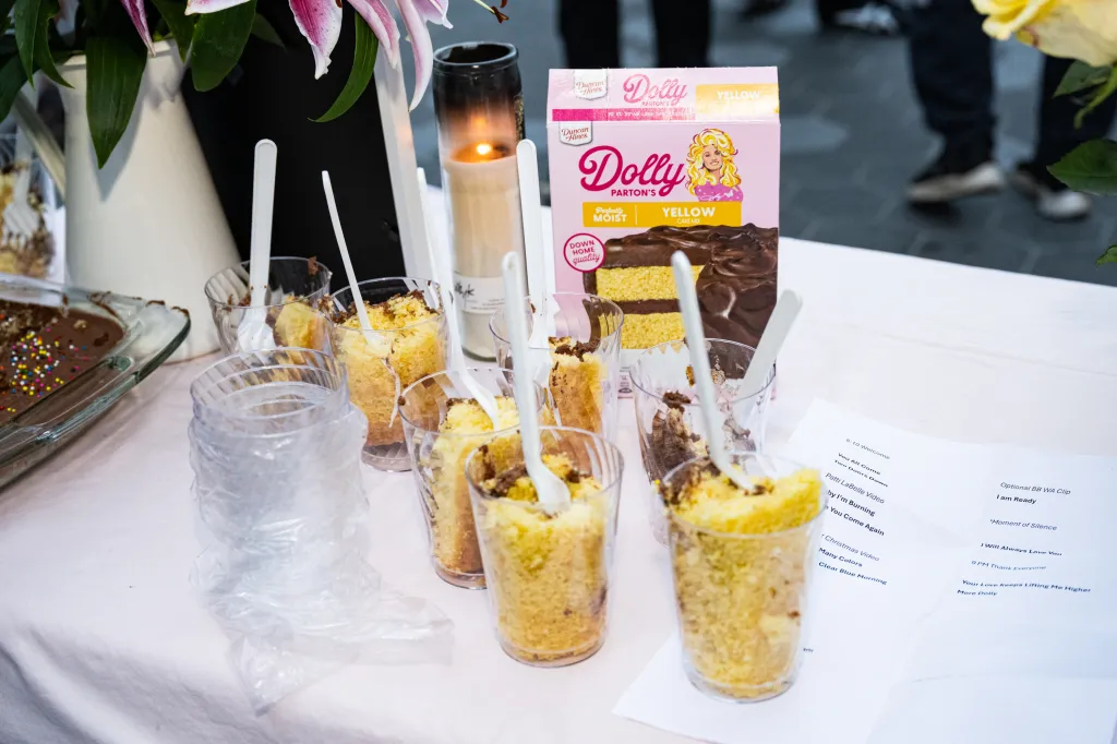 A Dolly Parton cake mix box next to individual servings of cake in plastic cups at a vigil.