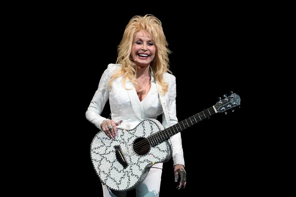 Dolly Parton performing on stage with a rhinestone-covered guitar.