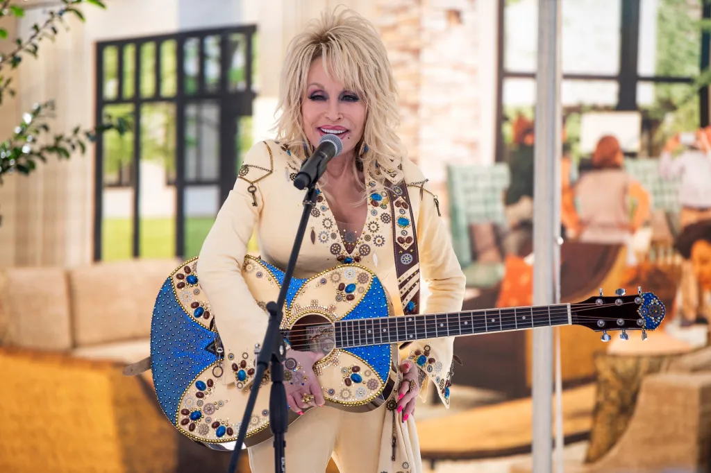 Dolly Parton playing a decorated guitar in front of a rendering of the Dollywood's HeartSong Lodge and Resort lobby.