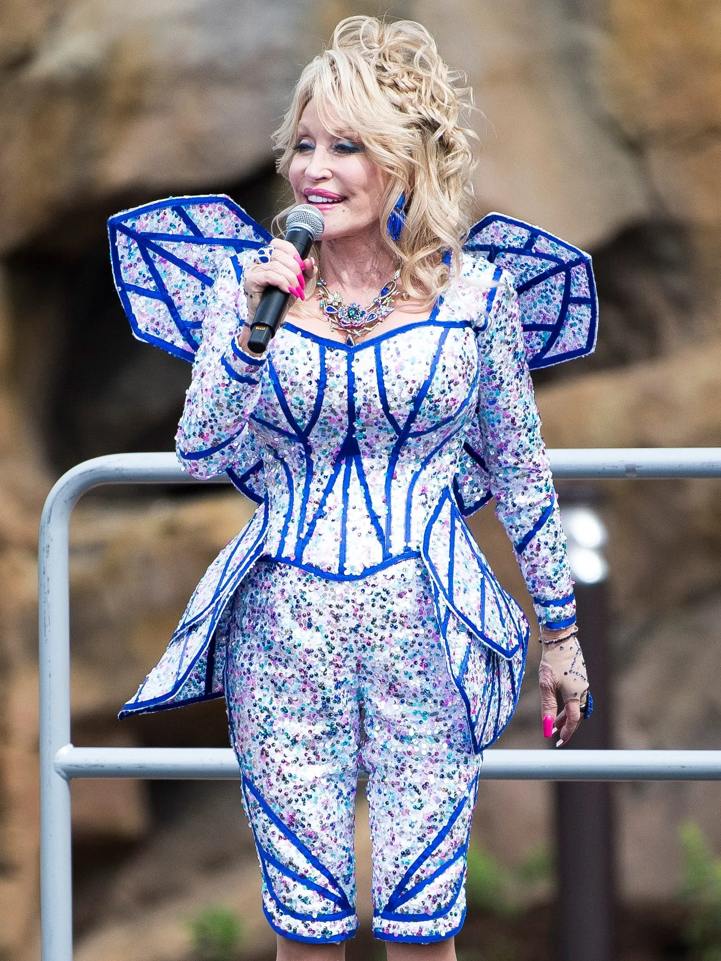 Dolly Parton speaks into a microphone at the grand opening of Dollywood's Wildwood Grove expansion.