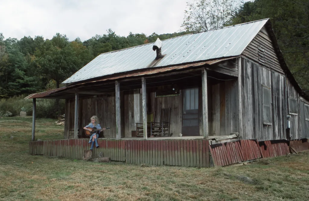 Dolly Parton, dressed in blue, sitting on a porch with a guitar.